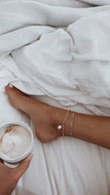 Model wearing turquoise beaded adjustable anklet layered with circular gold filled chain and single white fresh water pearl.
